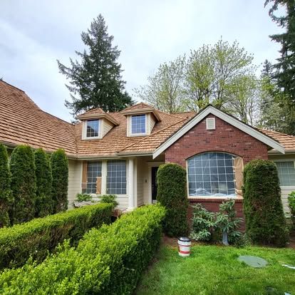 Brick house with dormer windows, arched front window, and manicured hedges in a green yard