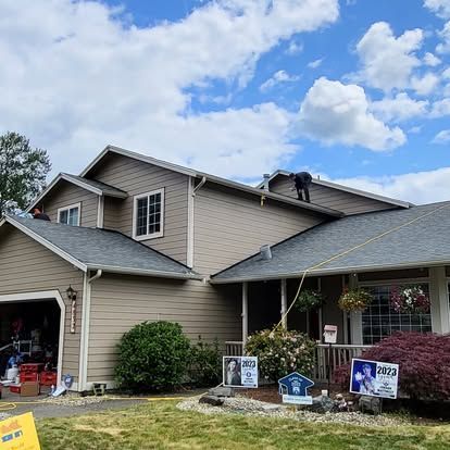 Suburban house with roof repair in progress and several yard signs in front.