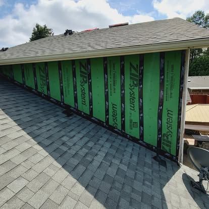 Partially reroofed house with gray shingles and exposed green waterproof sheathing on one side