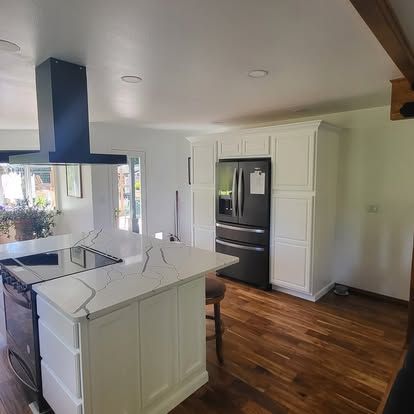 Bright kitchen with white cabinets, black appliances, wood floors, and a marble island