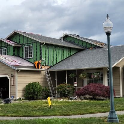 Worker on ladder repairing green siding on a suburban house under cloudy skies