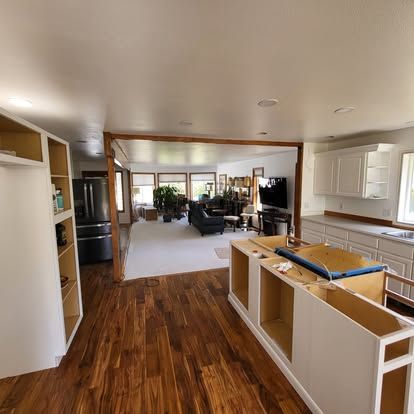 Bright open-plan kitchen and living room with wood floors and white cabinets, partially renovated.