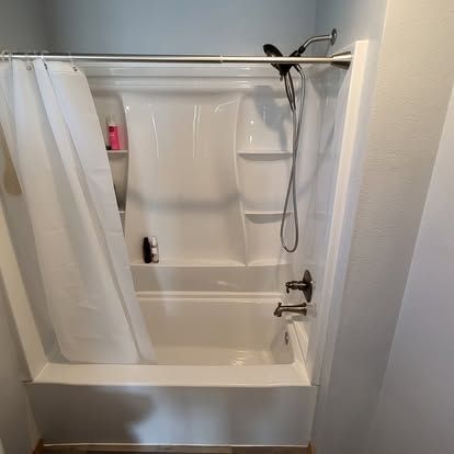 White bathtub and shower with closed curtain, handheld showerhead, and shelf in a bathroom