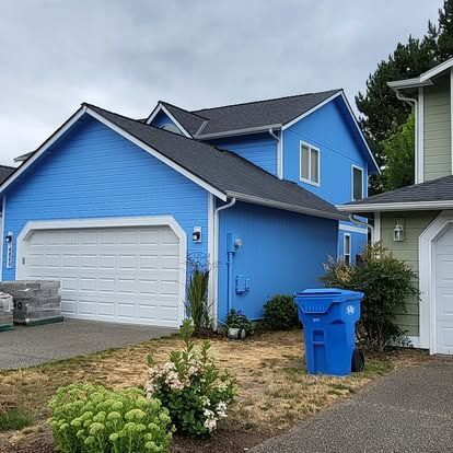 Bright blue two-story house with white garage door, driveway, and blue recycling bin in front yard