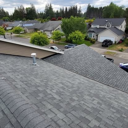 Rooftop view of a suburban neighborhood with gray shingles, trees, and houses under a cloudy sky