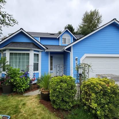 Blue house with white trim, front porch, garage, and landscaped yard under cloudy sky