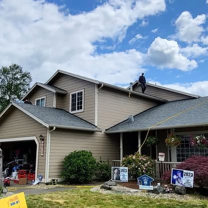 Suburban house with garage and yard signs, one person on the roof under a cloudy sky