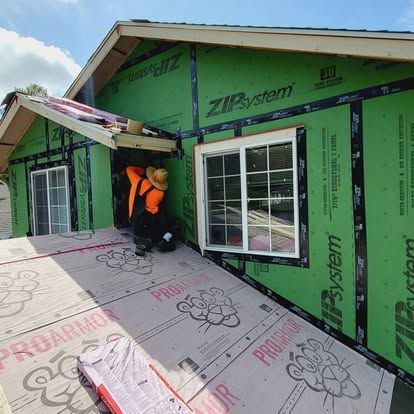Workers installing green house siding and windows on a partially finished home exterior
