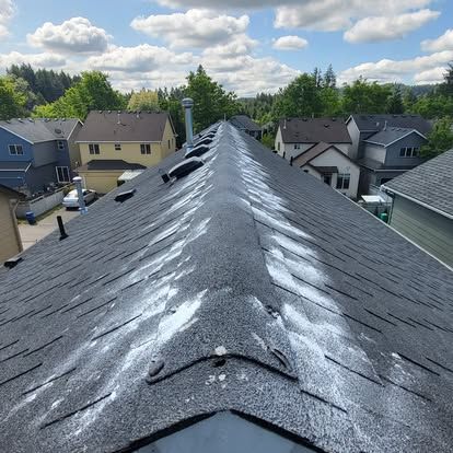 Roof ridge with gray shingles and several vents, viewed from above in a suburban neighborhood under a cloudy sky