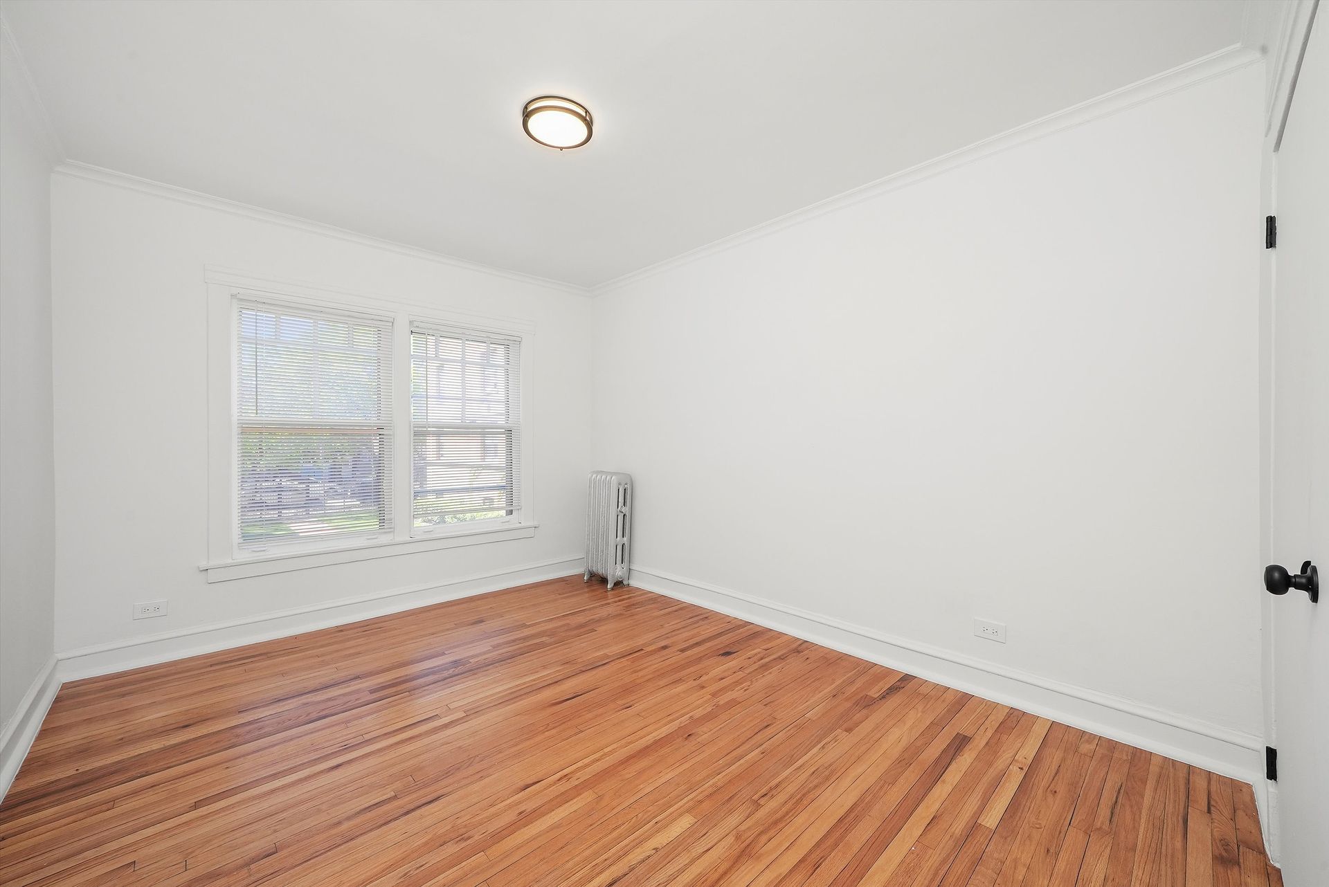 Empty room with hardwood floors, white walls, and a window.