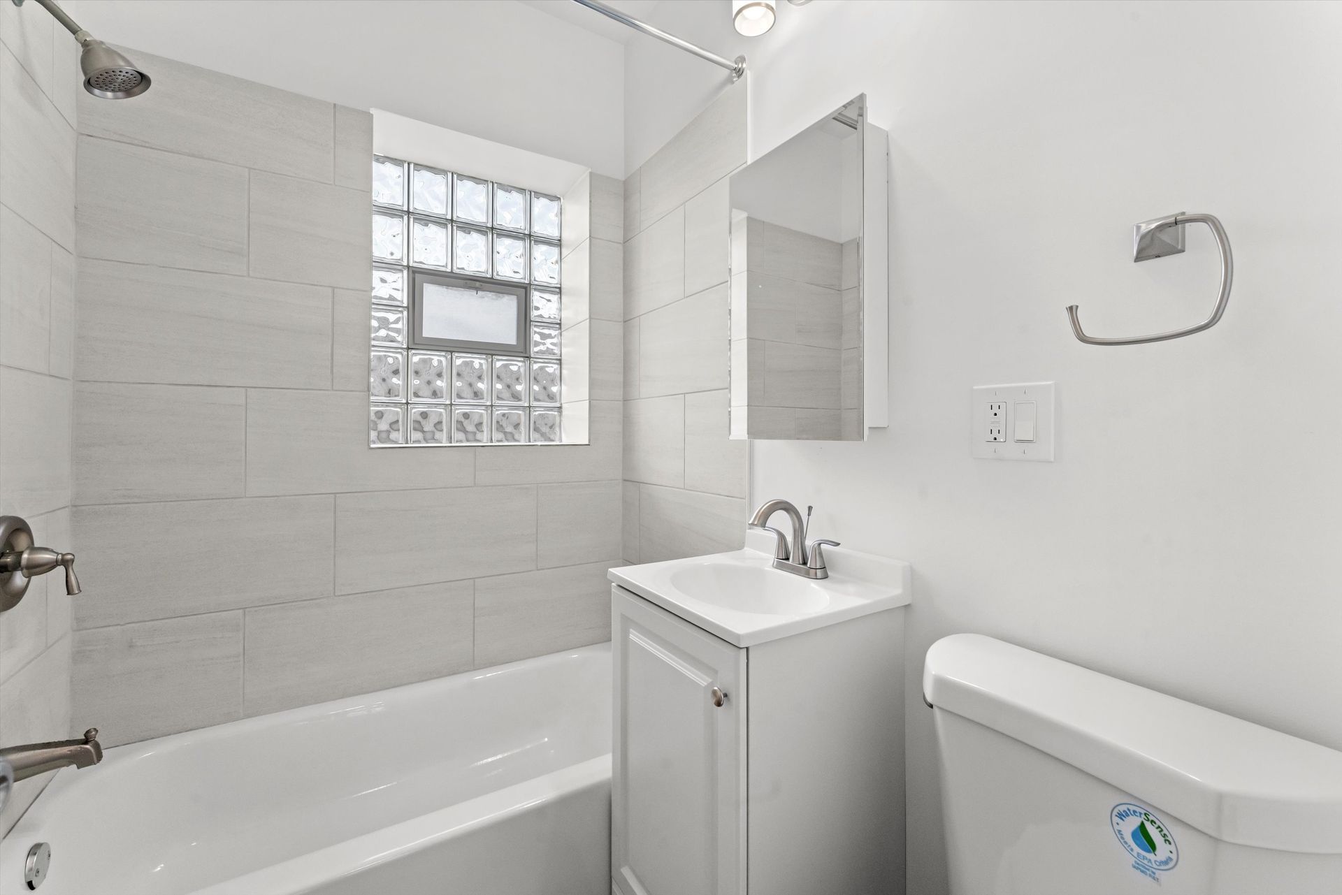 A small, bright white bathroom with a tub, sink, toilet, and window.