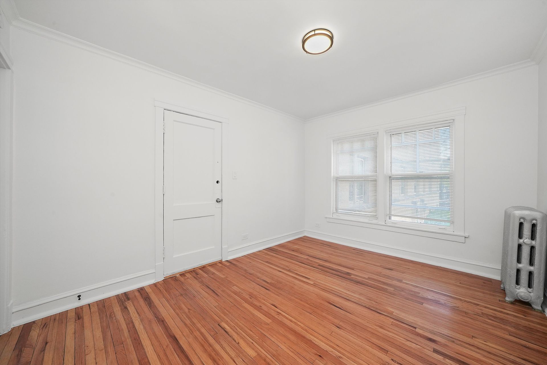 Empty room with hardwood floors, white walls, window, door, and radiator.