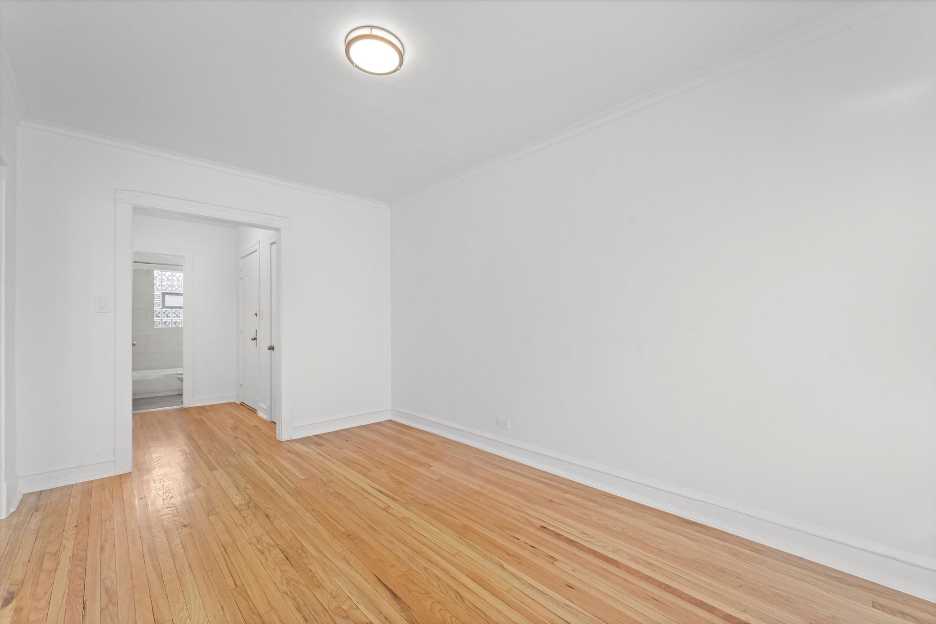 Empty room with hardwood floors, white walls, and an open doorway leading to a bathroom.