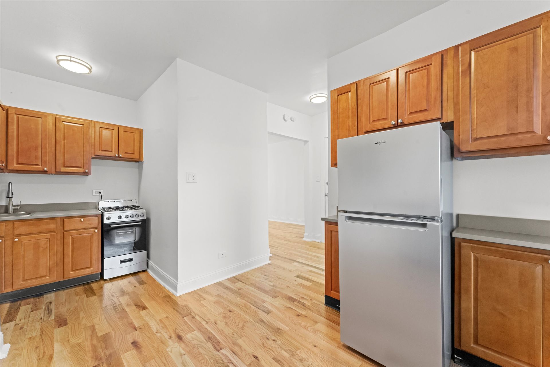 Kitchen with wooden cabinets, stainless steel fridge and stove. Wooden floors.