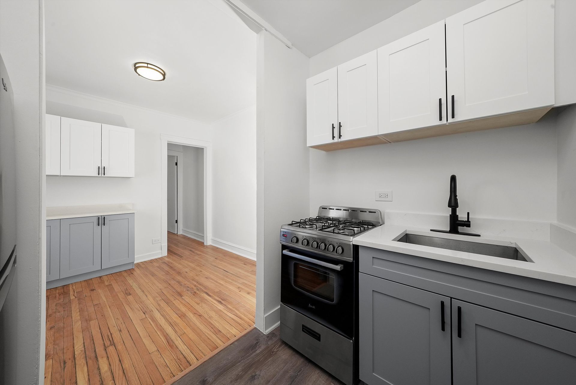 A small, modern kitchen with gray and white cabinets, gas range, and a view into a hallway.