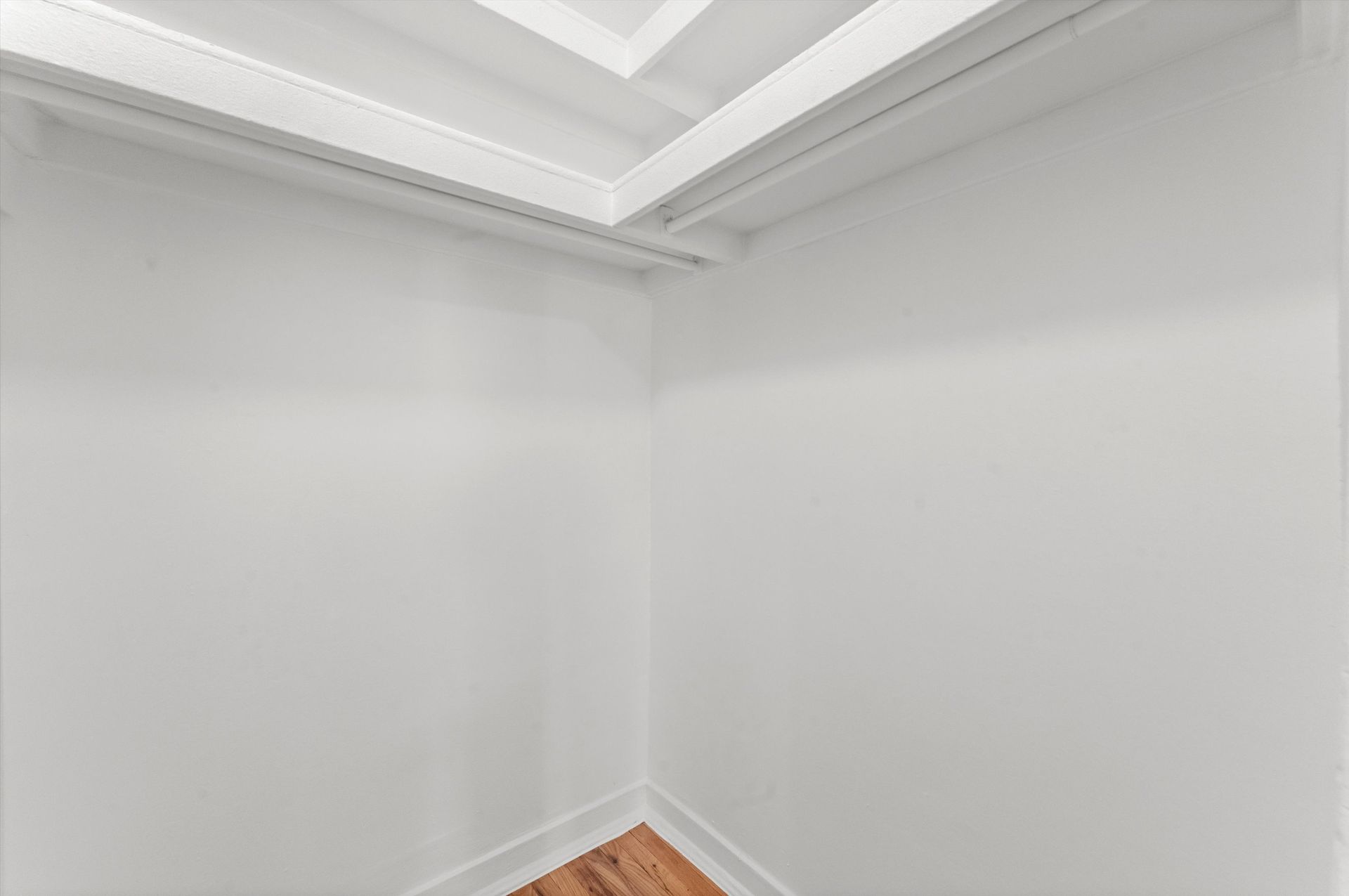Empty white closet corner with a clothes rod and wooden floor.