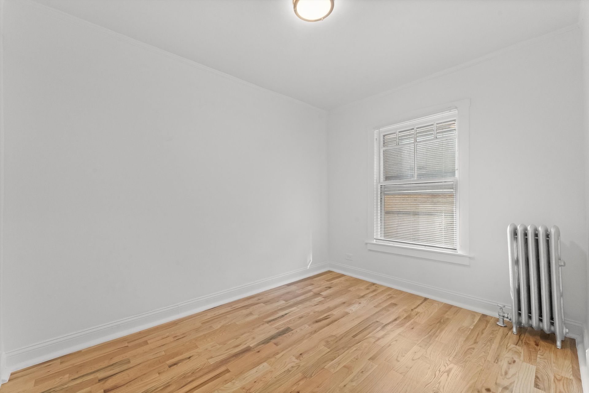 Empty room with hardwood floors, white walls, window, and radiator.