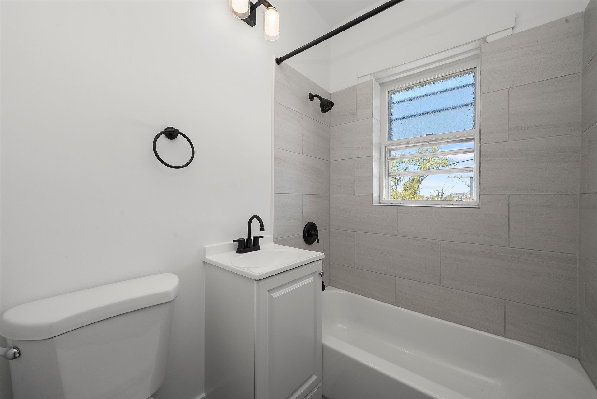 Bathroom with white fixtures, gray tile, and black accents.