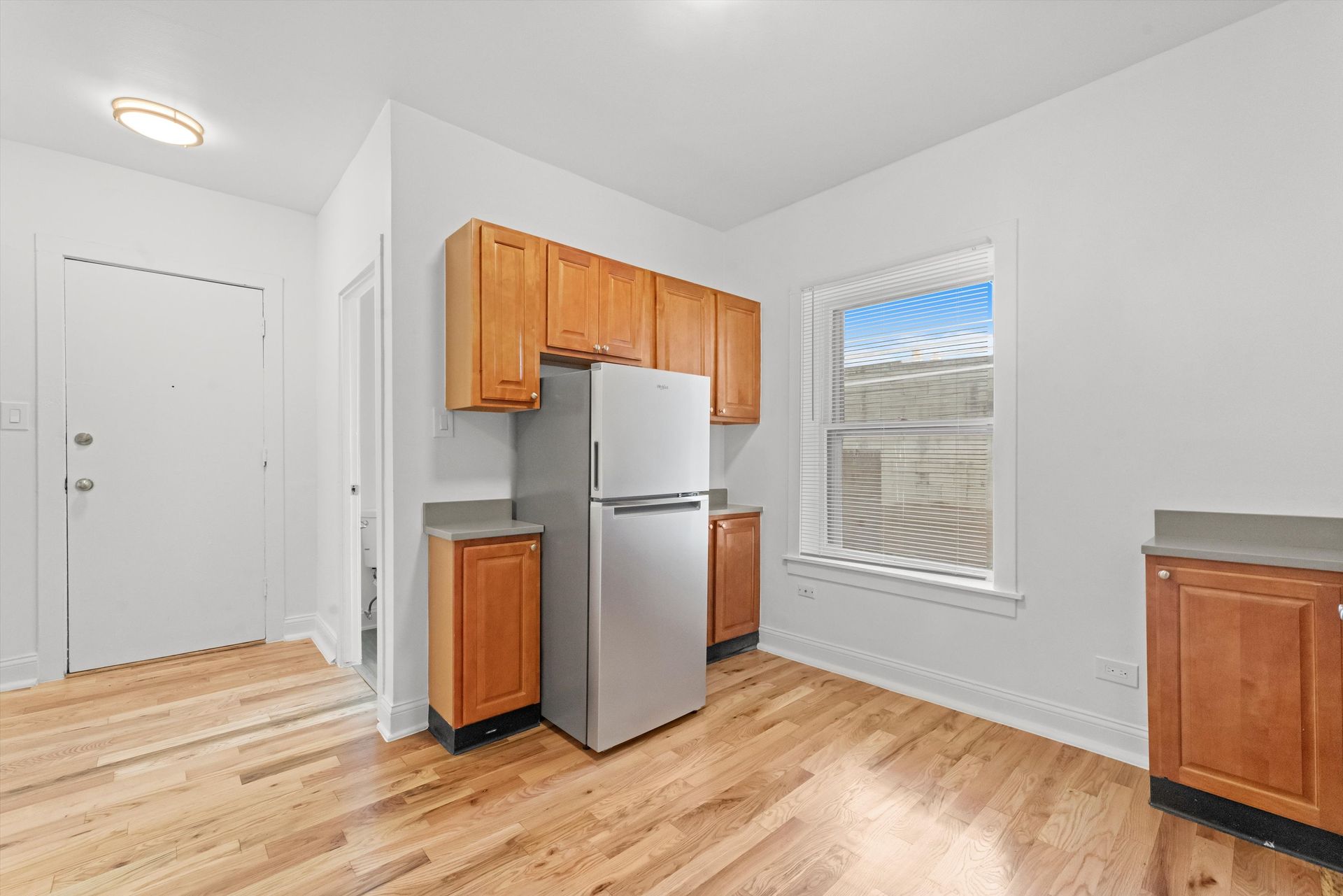 Kitchen with wood cabinets, stainless steel refrigerator, hardwood floors, and a window.