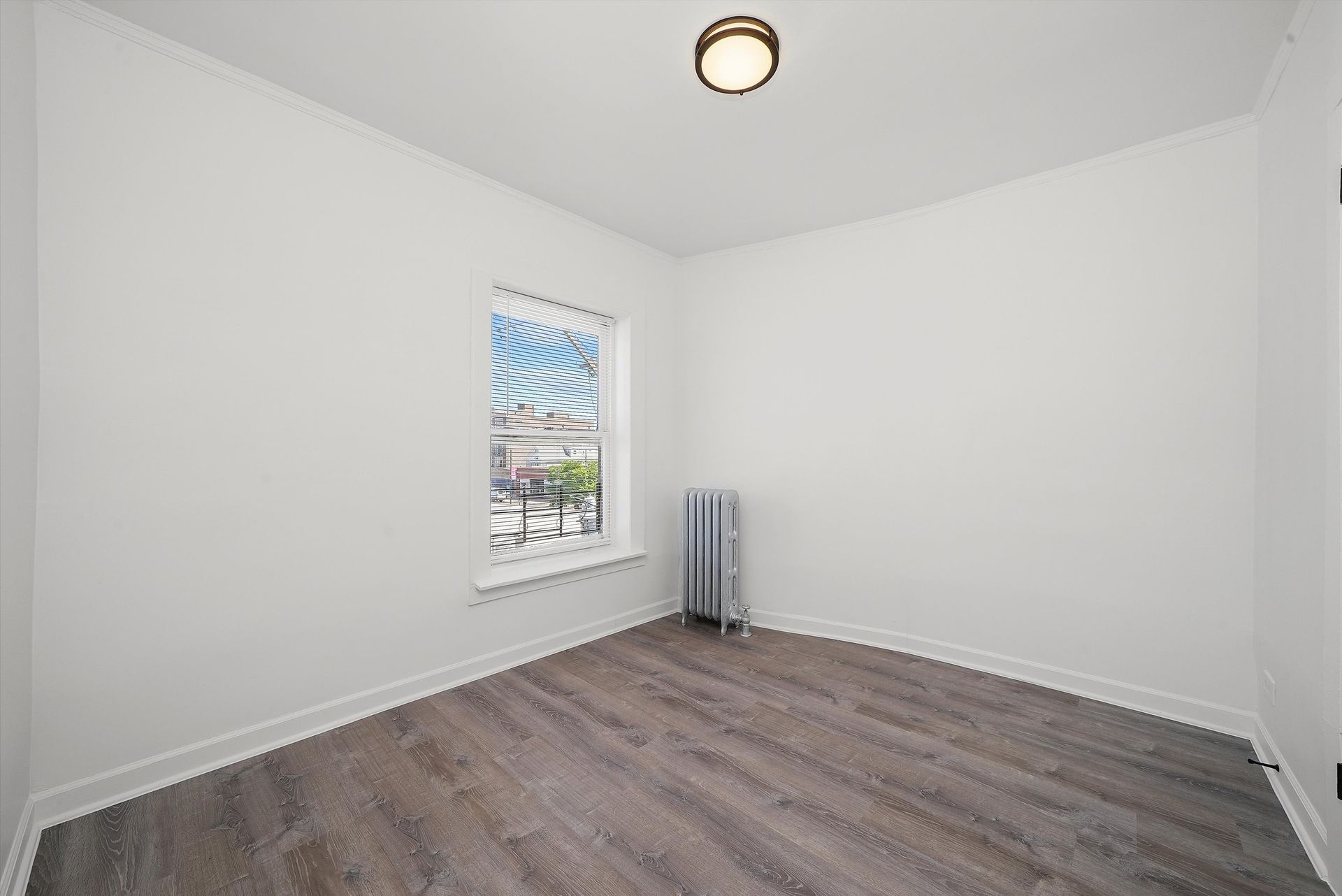 Empty room with gray wood-look flooring, white walls, small window, and a radiator.