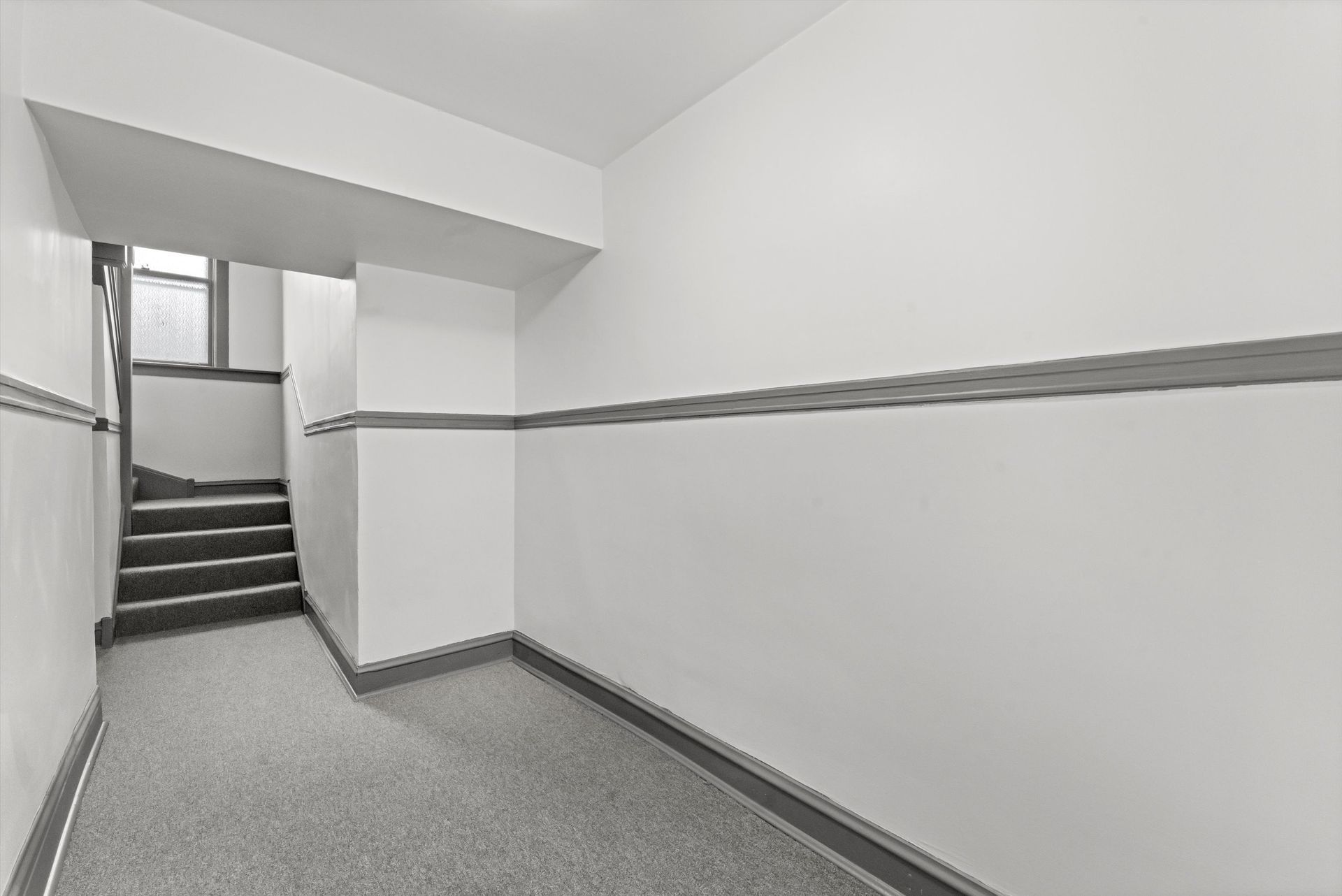 Hallway with stairs, carpeted floor, white walls with a gray stripe and baseboard.
