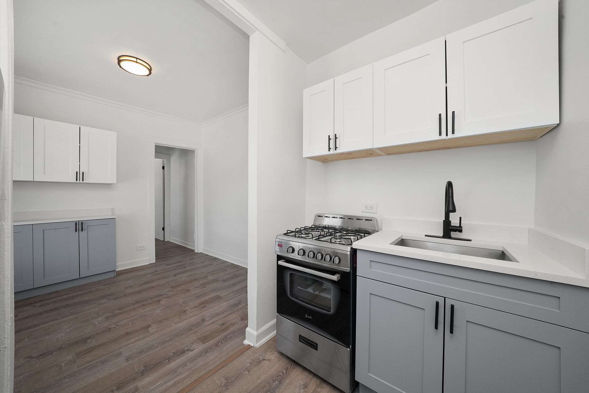 Kitchen with white cabinets, grey lower cabinets, stainless steel appliances, and light flooring.