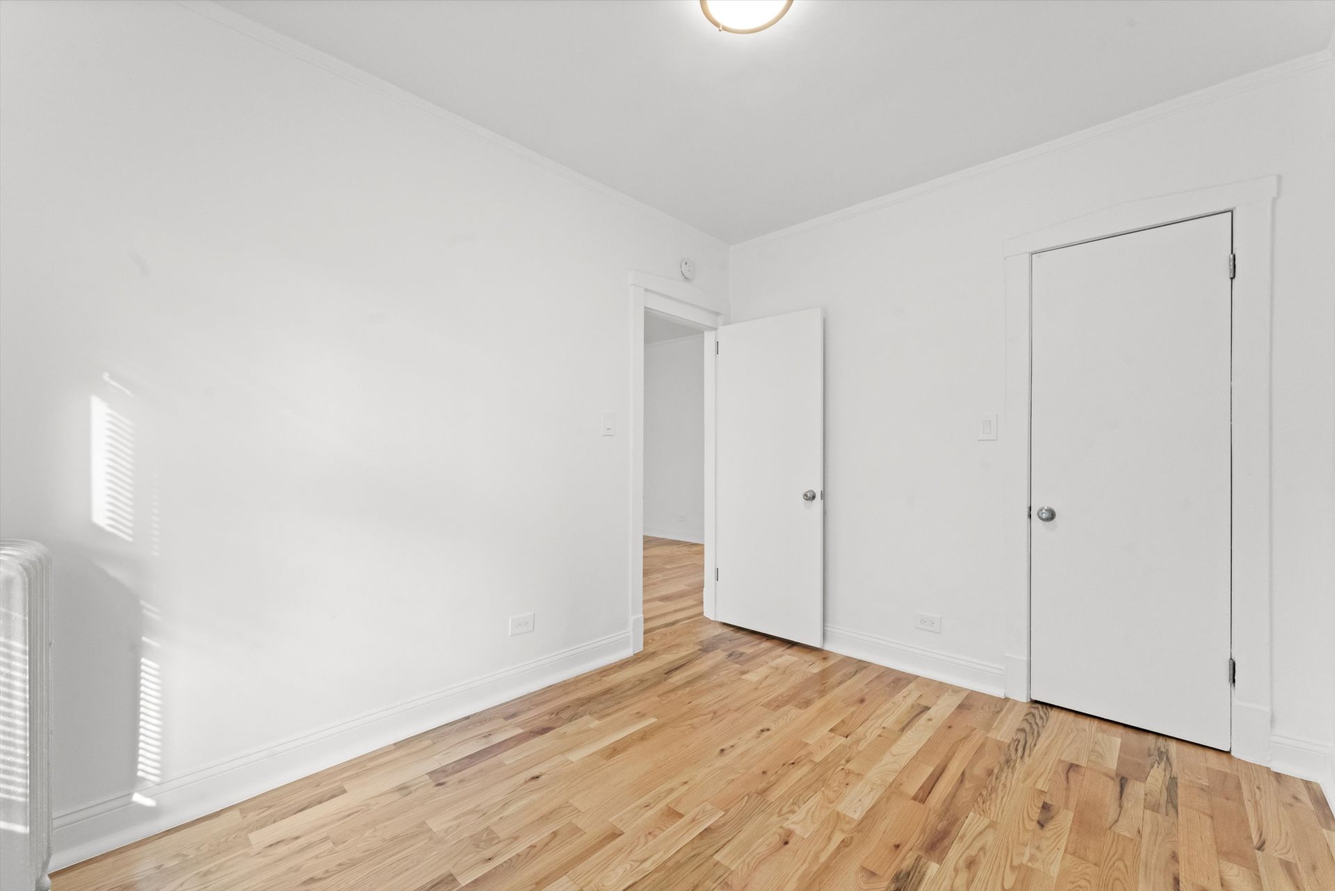 Empty bedroom with hardwood floor, white walls, and closed doors.