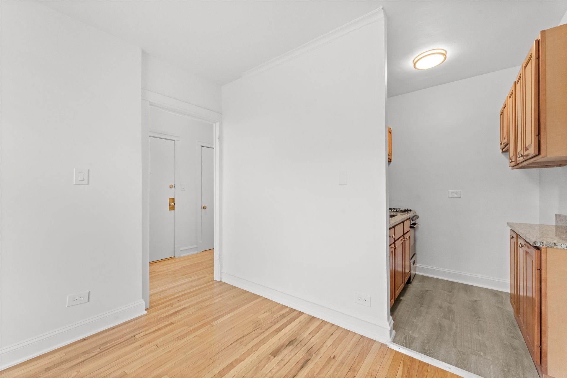Hallway leading to a kitchen, with wooden floors, white walls, and tan cabinets.