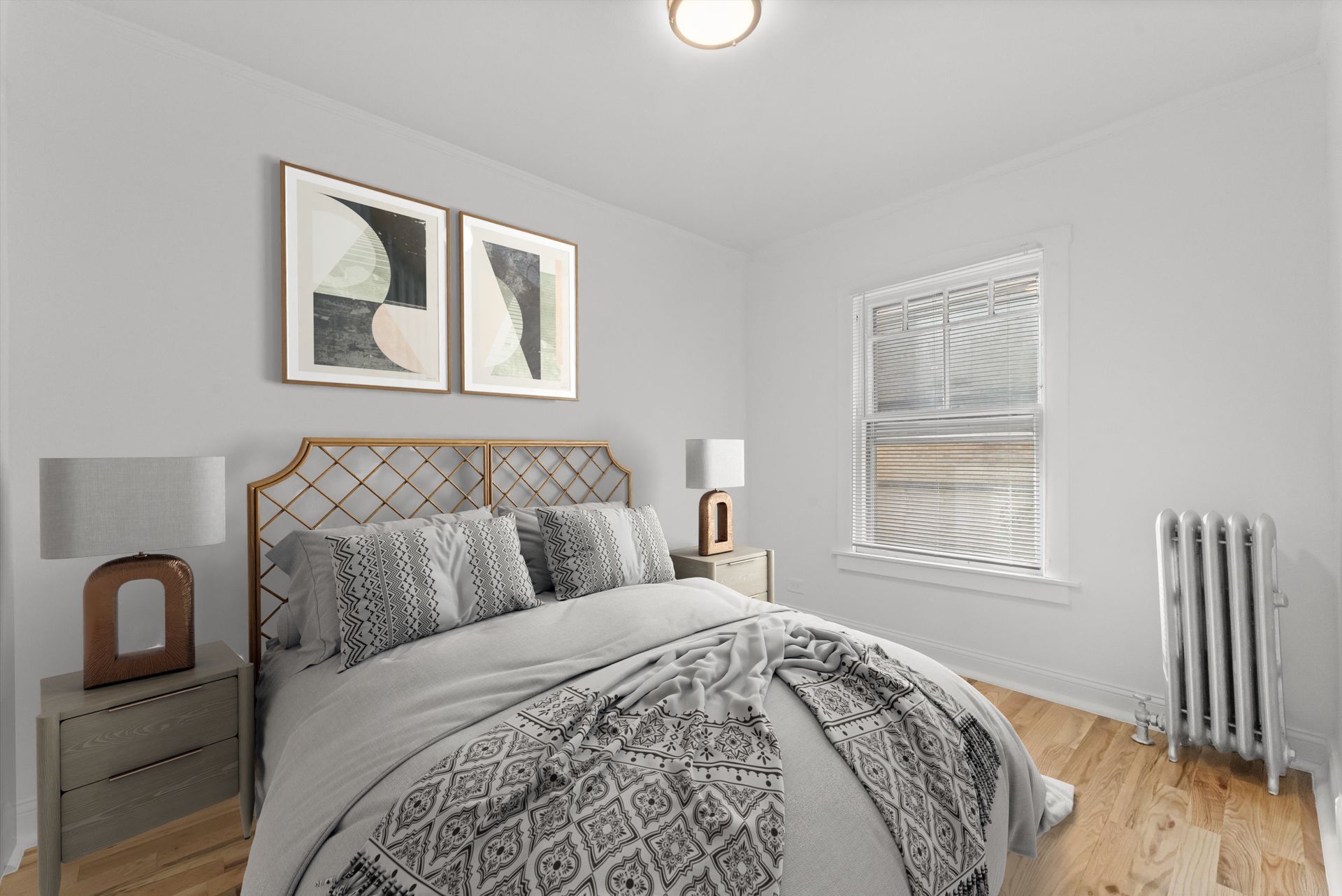 Bedroom with bed, nightstands, artwork, window, radiator. Light gray walls, natural wood floors, neutral tones.