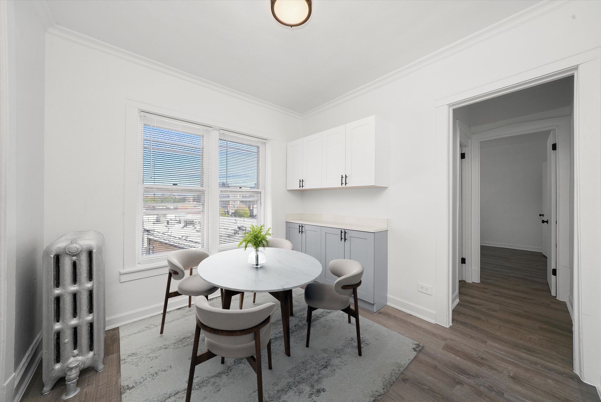 Small dining room with round table, four chairs, radiator, and window.