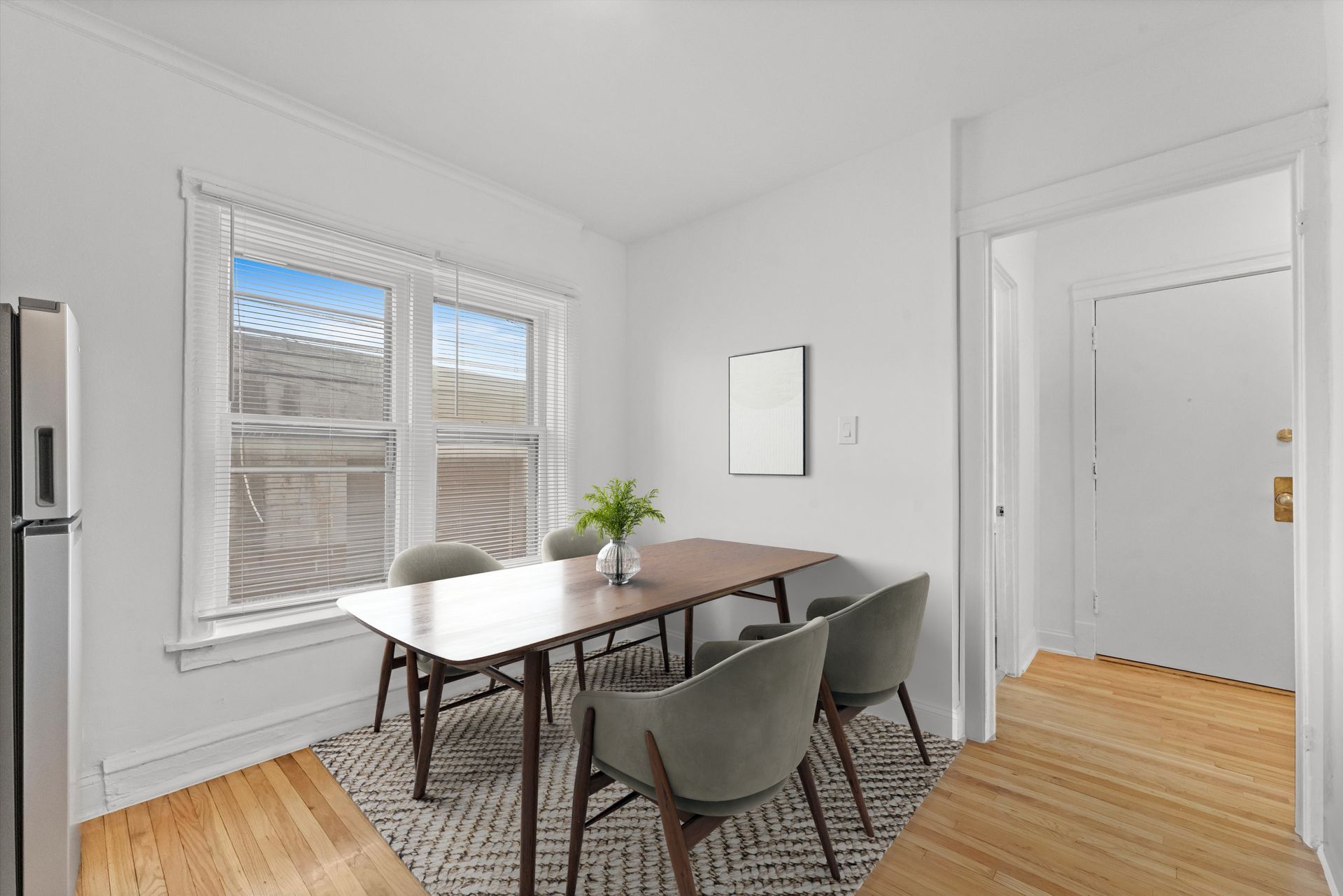 Dining area with table, chairs, window, and a doorway. Wooden floor and white walls.
