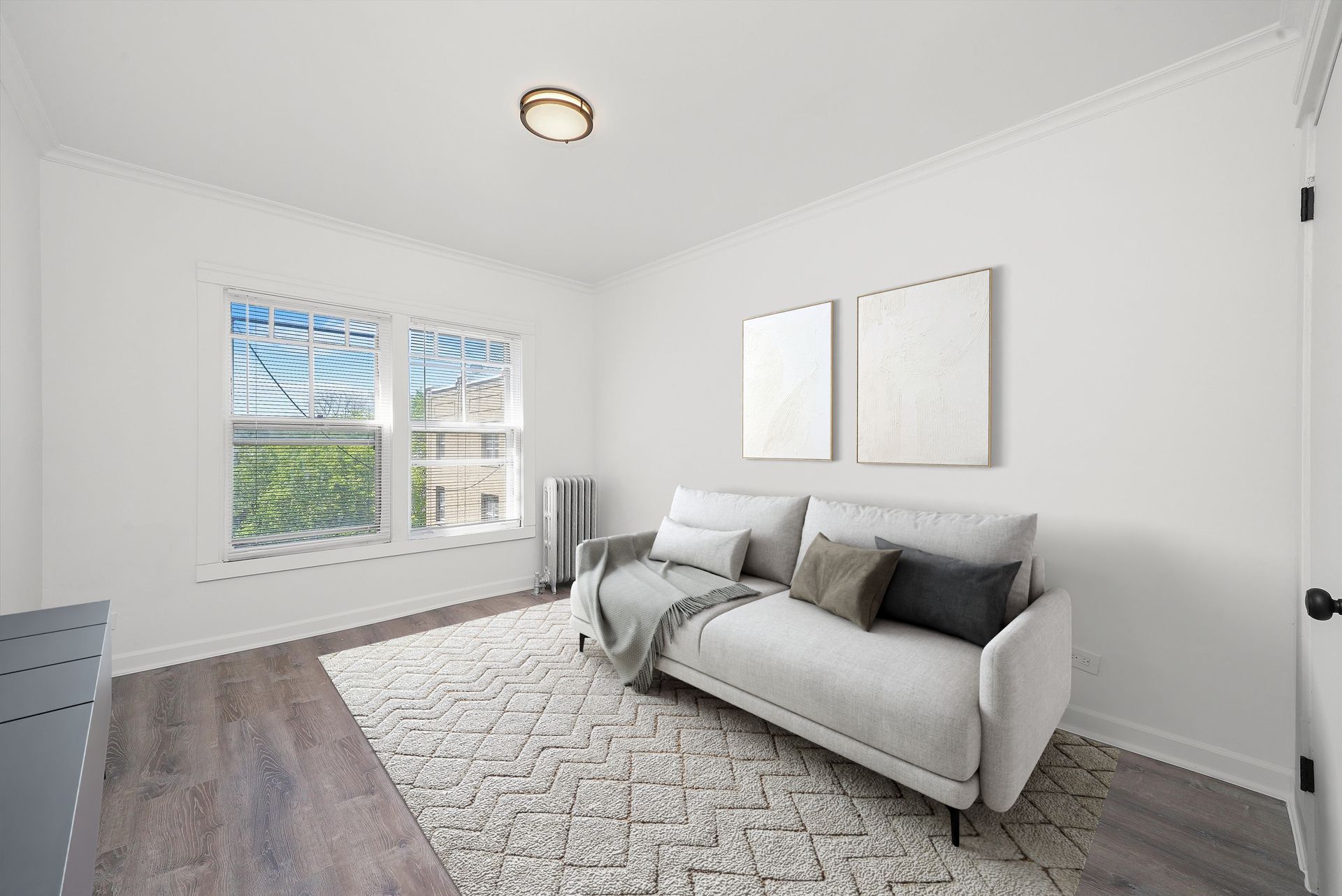 Cozy, bright room with a gray couch, rug, and two framed pictures on the wall near a window.