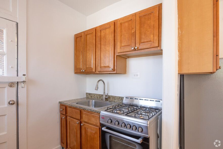 Small kitchen with wood cabinets, granite counter, gas stove, and stainless steel refrigerator.