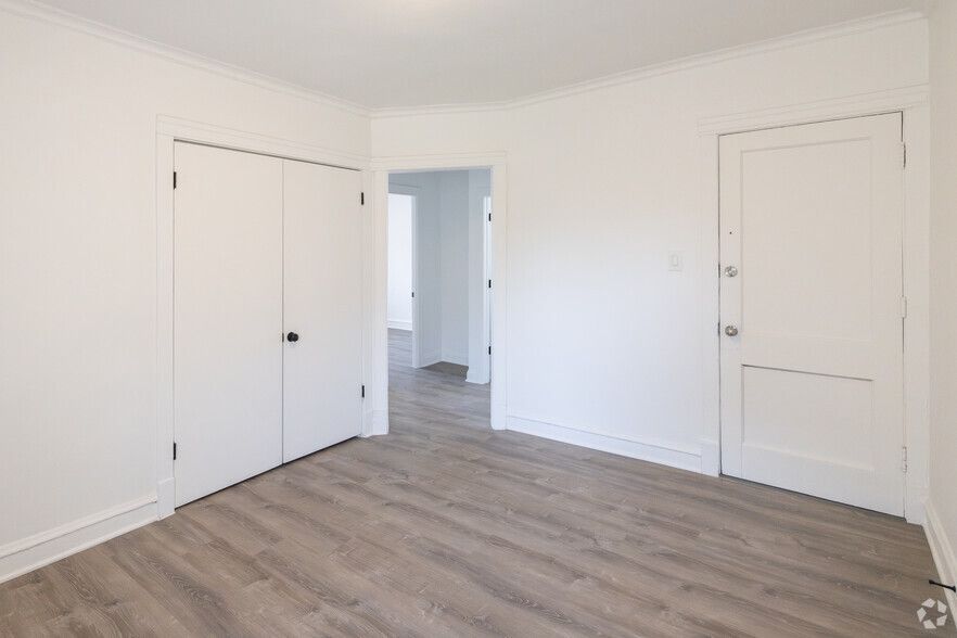 Empty room with white walls, two closets, and wood-look flooring. Doorway leads to a hallway.