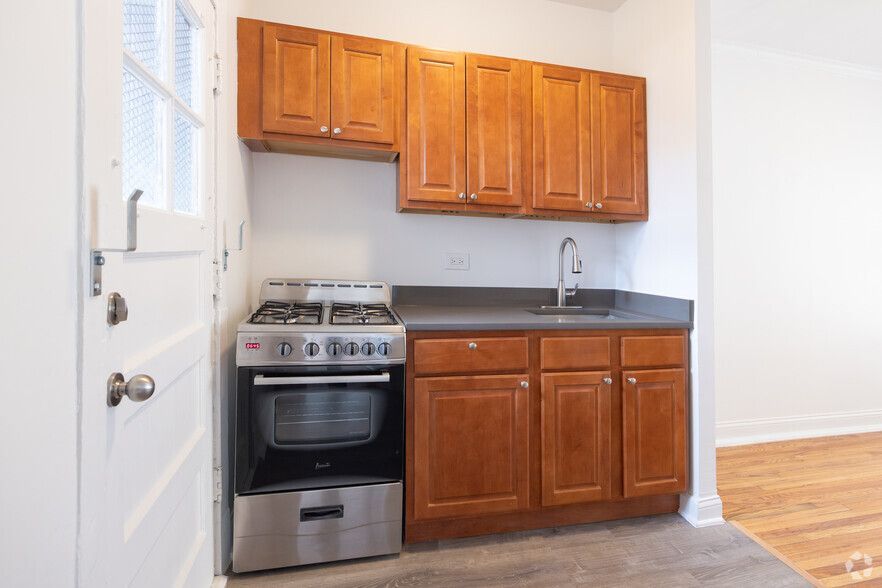 Small kitchen with wood cabinets, stainless steel stove, and sink next to a white door.