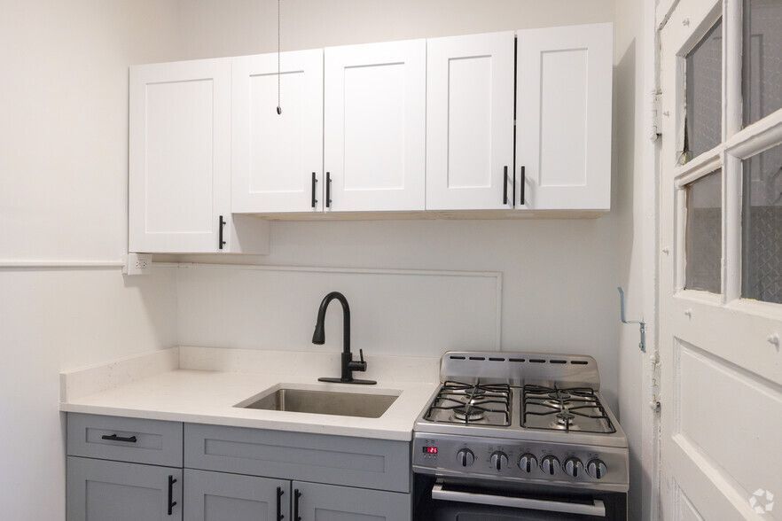 Small kitchen with white and gray cabinets, stainless steel stove, and sink.