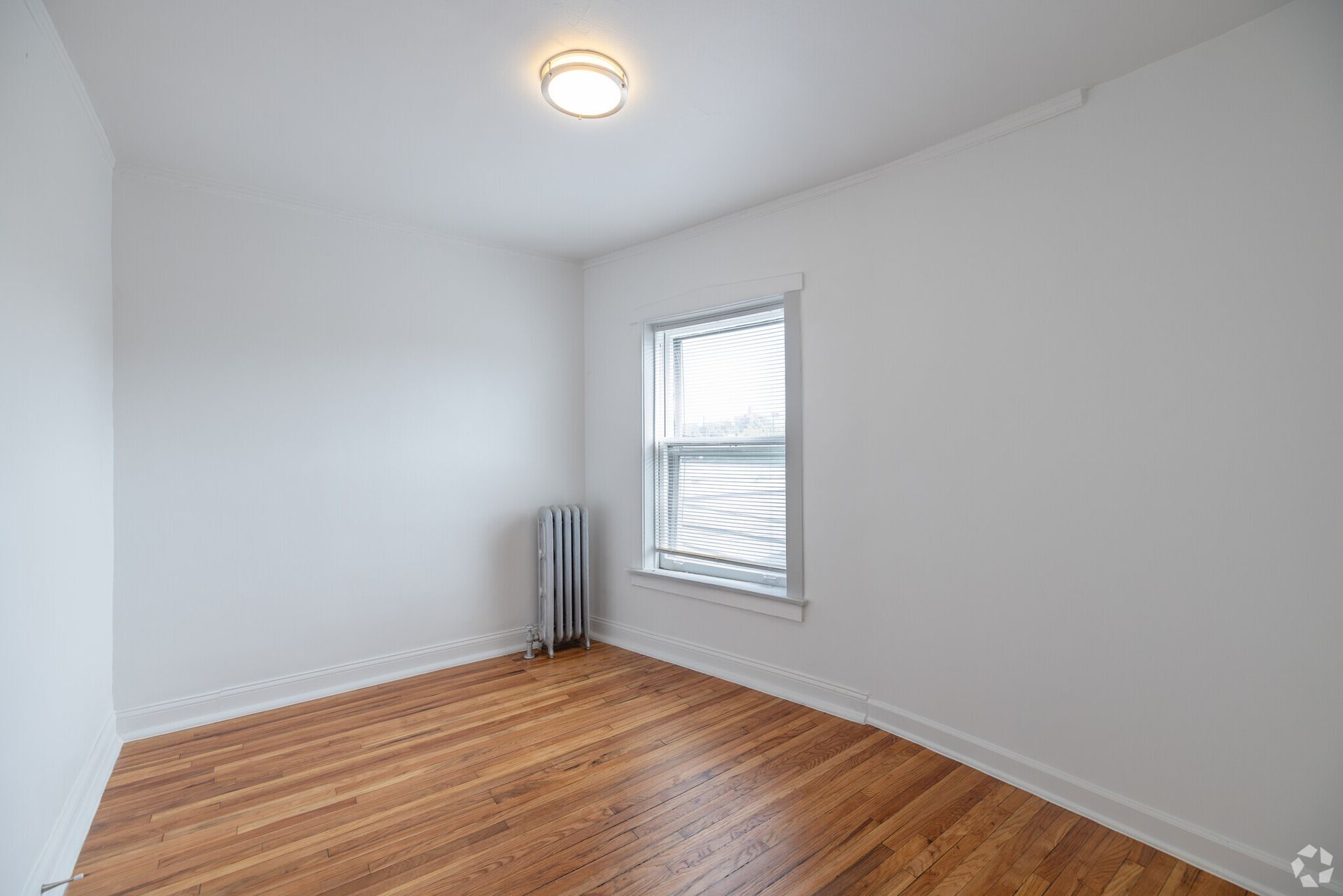 Empty room with wood floors, white walls, window, and radiator.