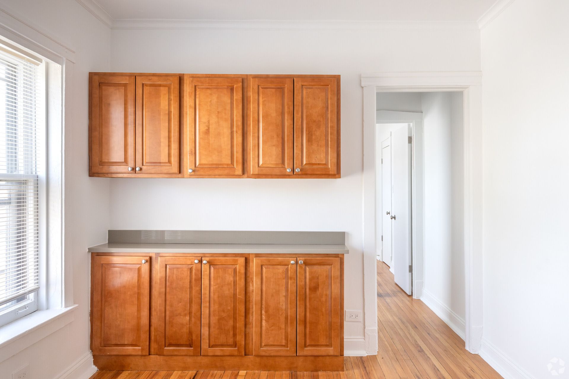Wooden kitchen cabinets against white walls, next to a window and doorway.