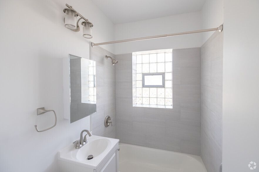 Bright white bathroom with a tub, sink, and a window.