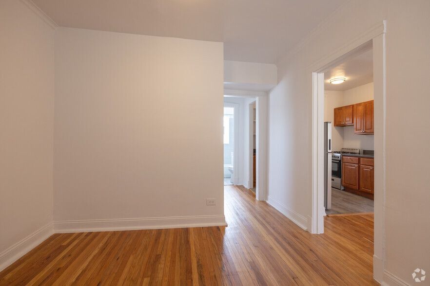 Empty apartment hallway with wooden floors, white walls, and doorways to other rooms.