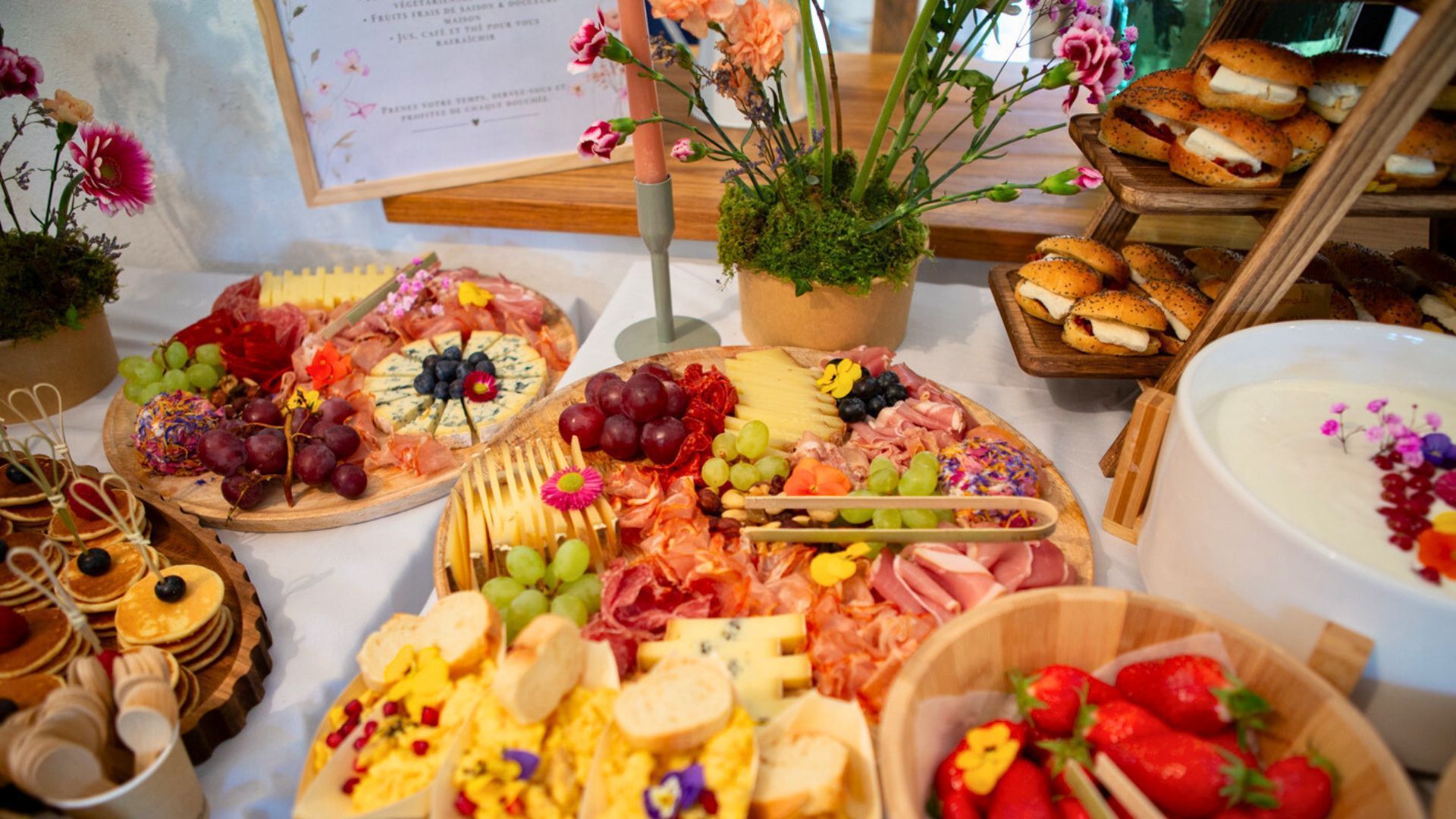 Un somptueux buffet composé de planches de charcuterie assorties, de sandwichs, de fruits frais et de pâtisseries, présenté sur une table blanche.