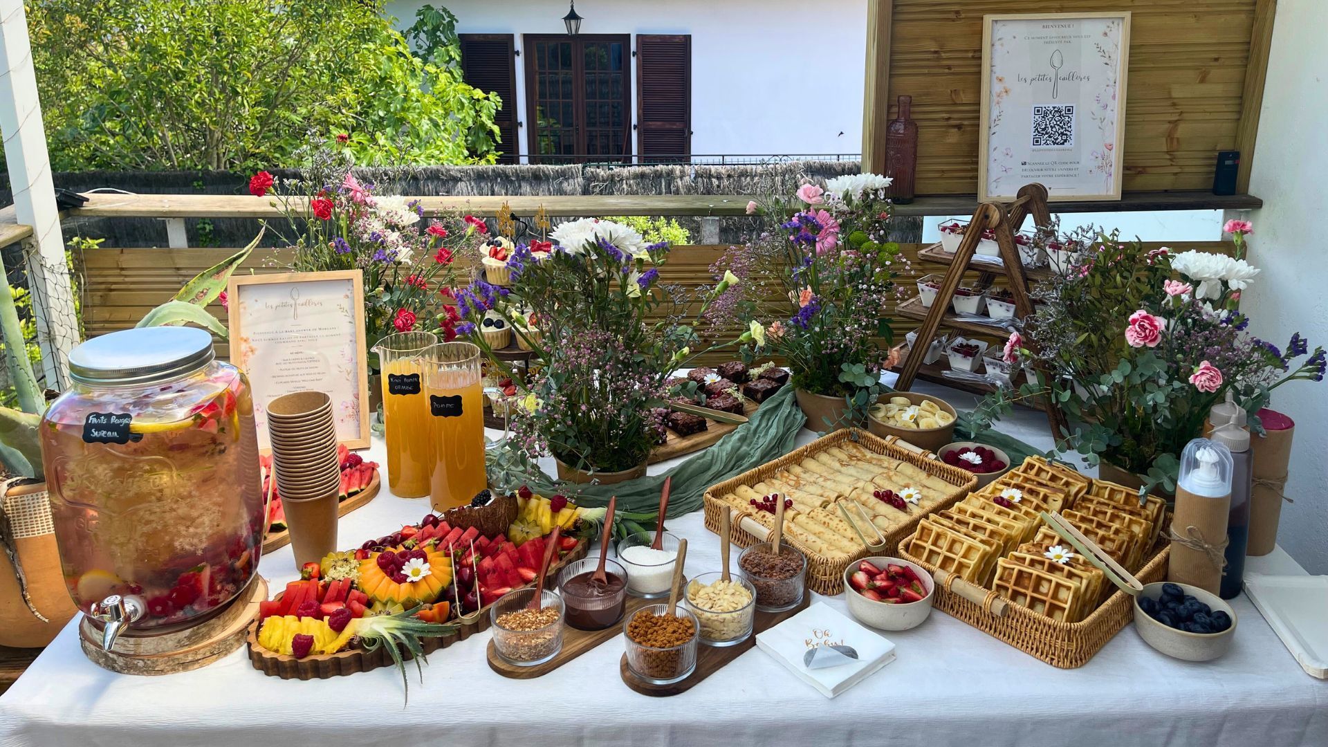 Un buffet de brunch proposant des fruits, des gaufres, des fontaines à jus et des compositions florales sur une terrasse extérieure.