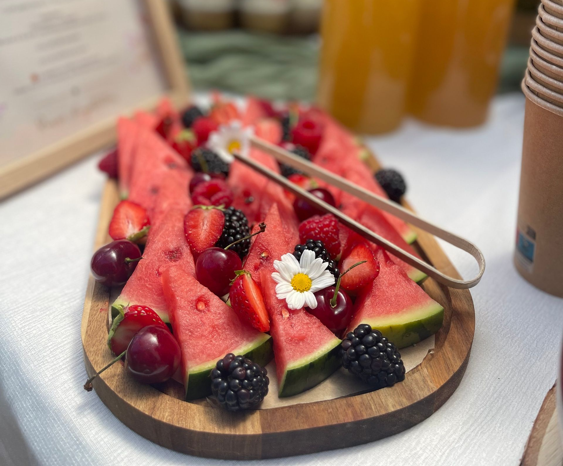 Un plat de service en bois garni de tranches de pastèque, de cerises, de mûres, de fraises et de fleurs blanches.