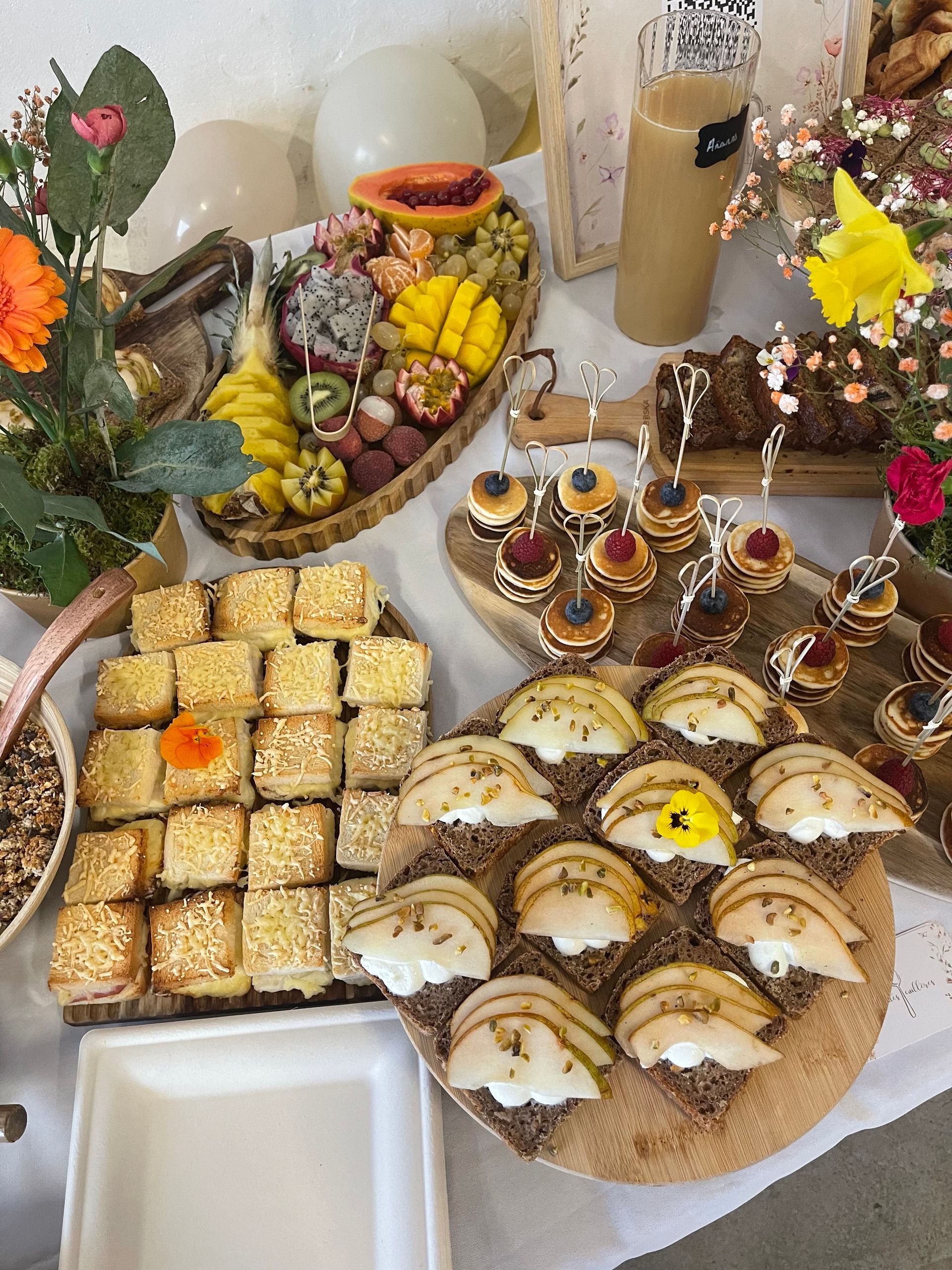 Vue en plongée d'un buffet festif composé de fruits, d'amuse-gueules sur des planches en bois, de petits sandwichs et de fleurs fraîches.