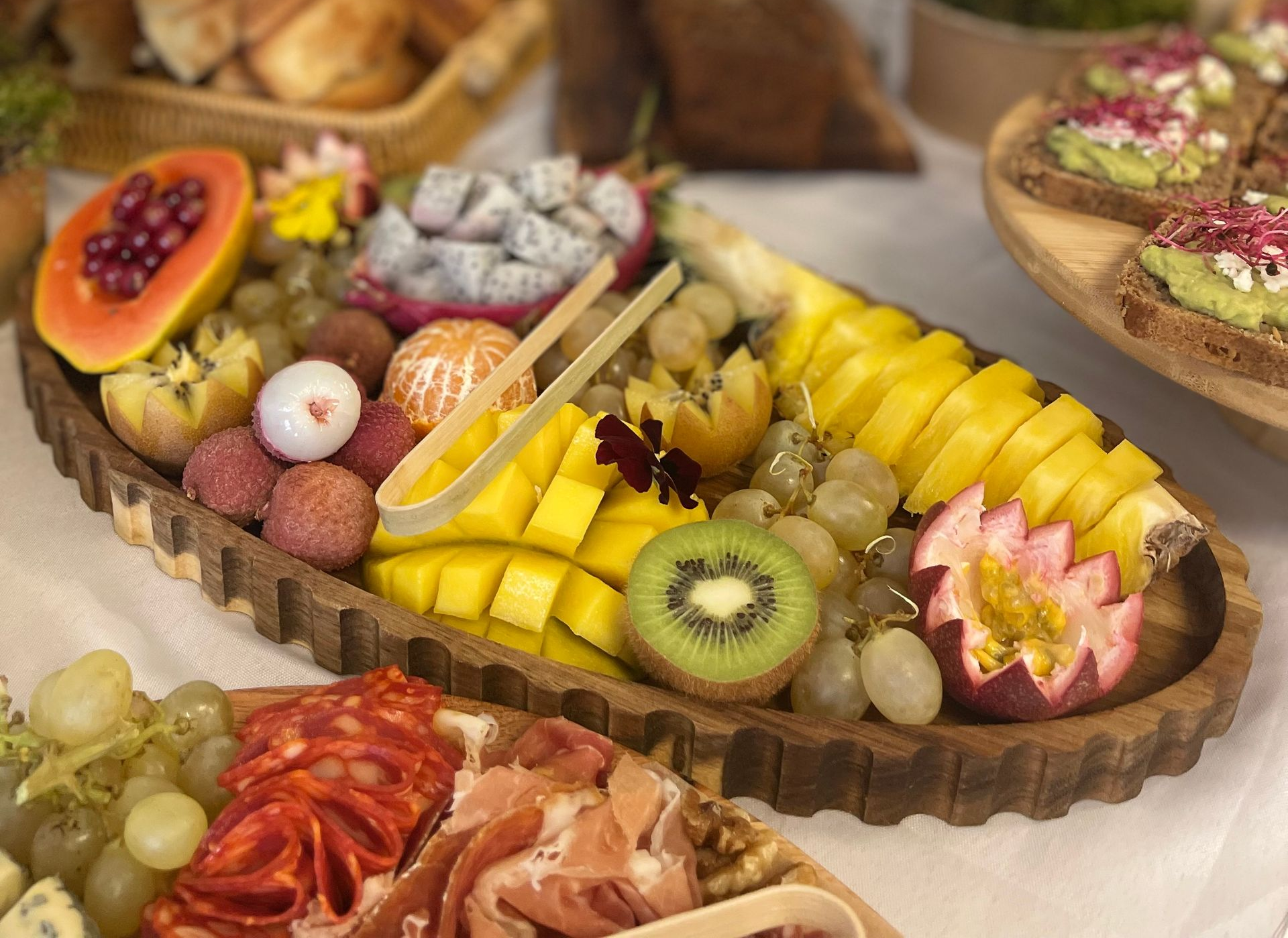 Un plateau en bois garni de fruits frais colorés, notamment de la mangue, du kiwi, du fruit du dragon, de la papaye et du raisin coupés en tranches.