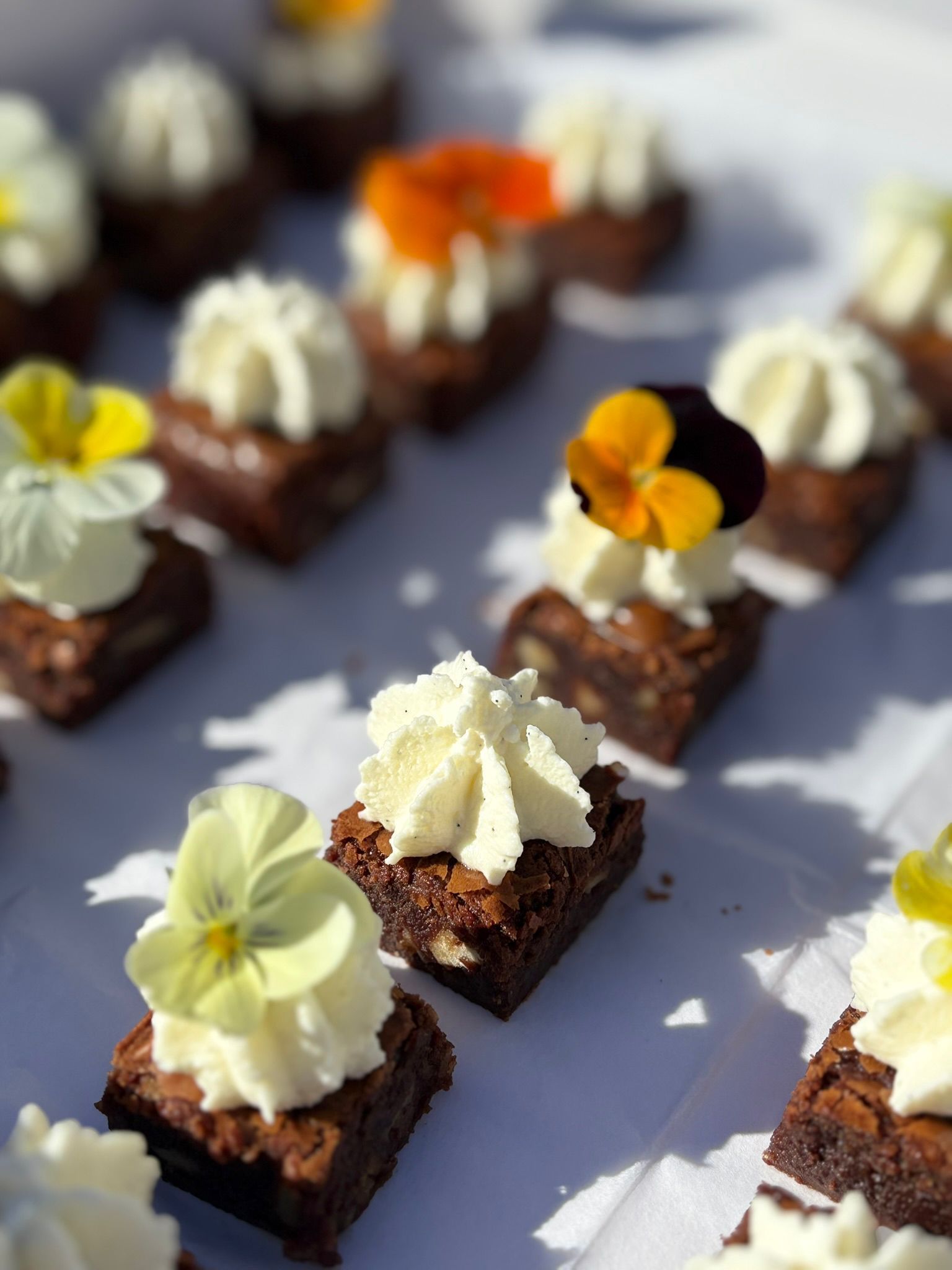 Un plateau de service en bois à trois étages garni de brownies au chocolat, de fraises fraîches et de petites fleurs.