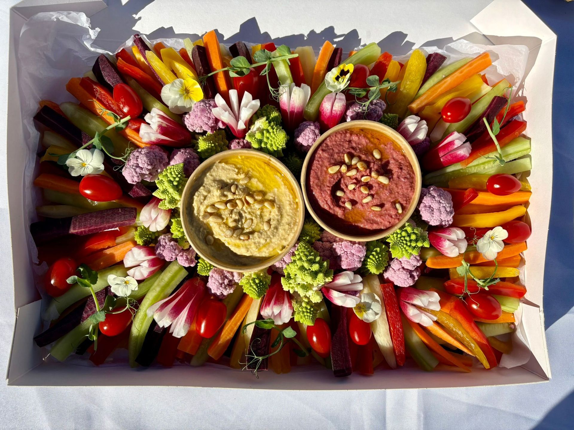 Un buffet de petit-déjeuner garni de bols de granola, de fruits, de viennoiseries et de charcuterie, décoré de fleurs fraîches.