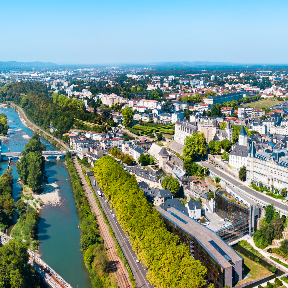 Vue aérienne d'une ville au bord d'une rivière, avec un pont, une végétation luxuriante et un complexe de château historique.
