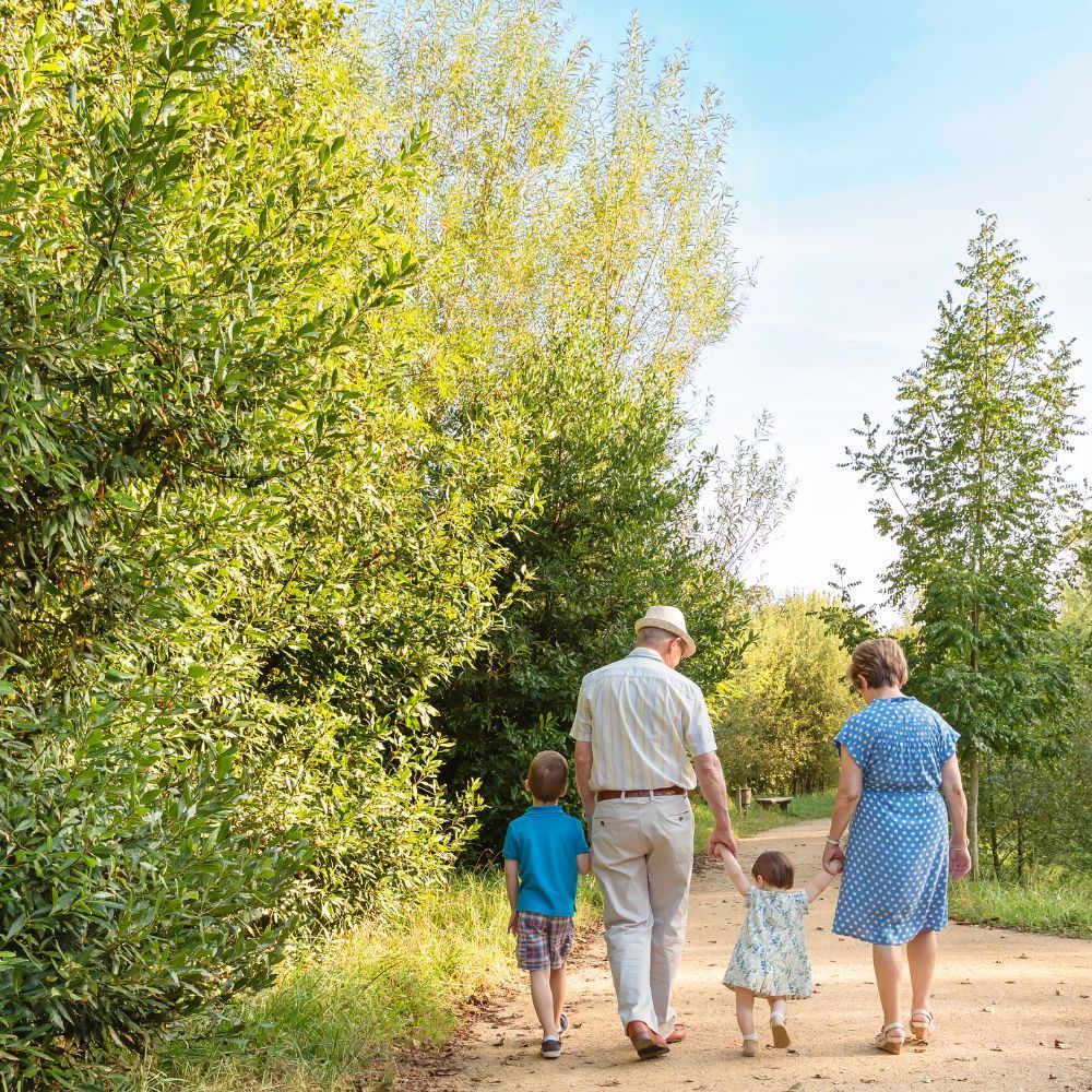 Une personne et deux enfants marchent main dans la main le long d'un chemin de terre bordé d'arbres, tandis qu'une autre personne marche à leurs côtés.