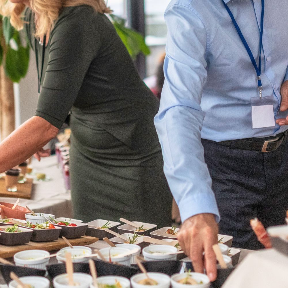 Des personnes se servent dans de petits bols de nourriture sur une table de buffet lors d'un événement professionnel.